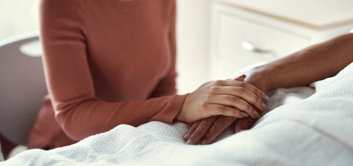 A woman holds hand with her dying family member in the hospital