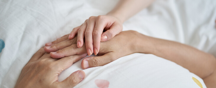 a person places their hands on the hands of a person in a hospital bed