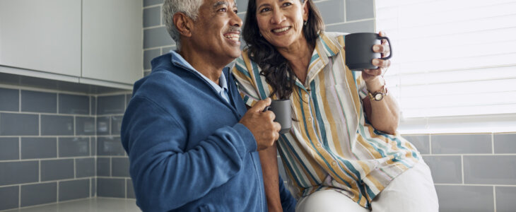 A joyful senior couple sitting on a kitchen counter, drinking coffee and sharing a loving moment.